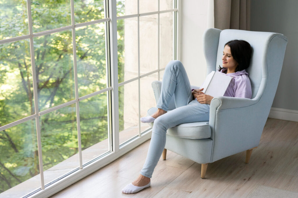 A person is holding a book while looking out of a large, floor-to-ceiling window.