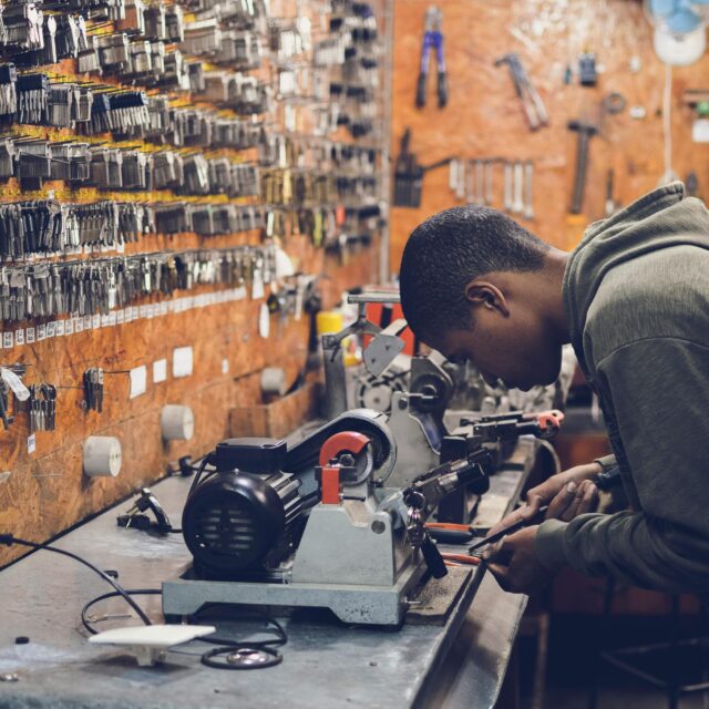 Young technician repairing equipment in a cluttered workshop filled with tools on the walls and a workbench.