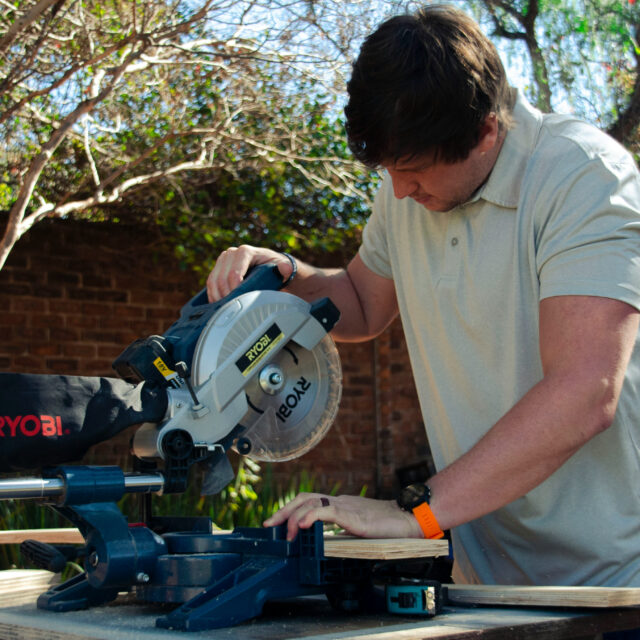 Man cutting wood with a circular saw in an outdoor setting.