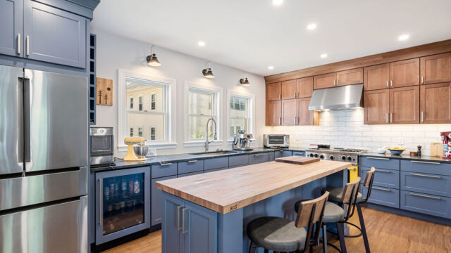 Modern kitchen with wooden island, bar stools, blue cabinetry, stainless steel appliances, and under-cabinet lighting.