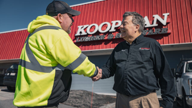 Two men shaking hands in front of Koopman Lumber and Hardware building.