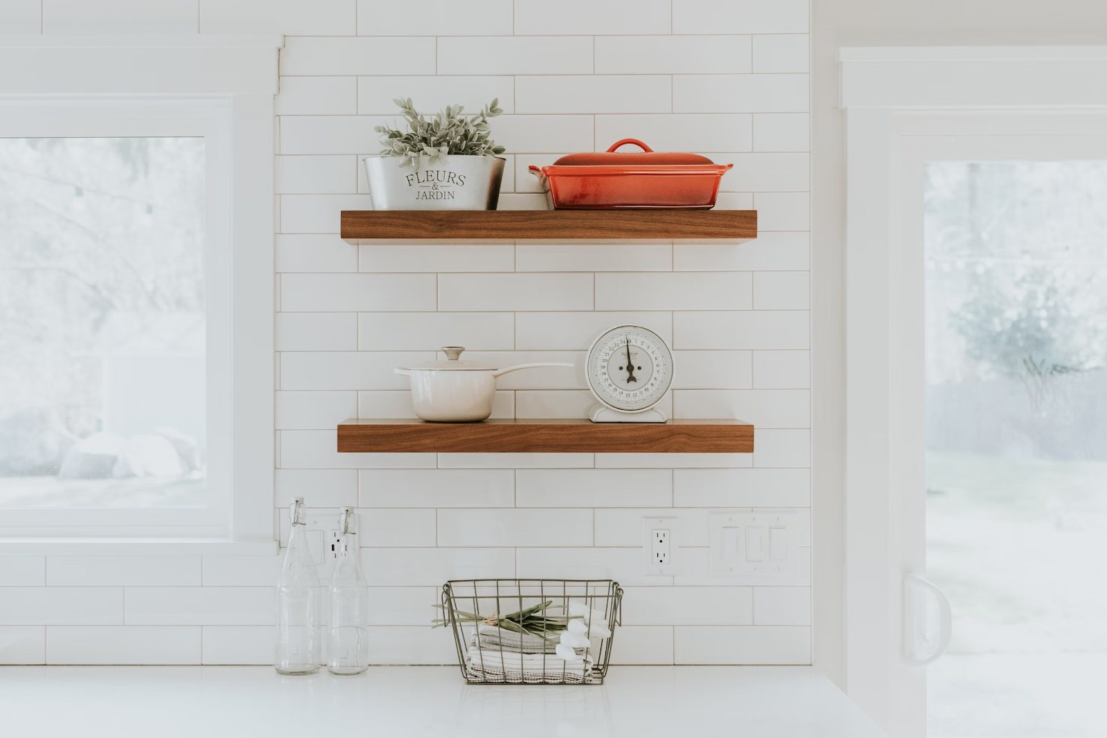 This image depicts a kitchen with two wooden open shelves that display ceramic cookware, a scale, and a flower pot. 
