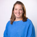 Smiling person in a blue sweater posing against a neutral background.