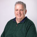 Smiling person in a green sweater against a plain background.