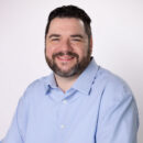Smiling person in a light blue shirt against a white background.