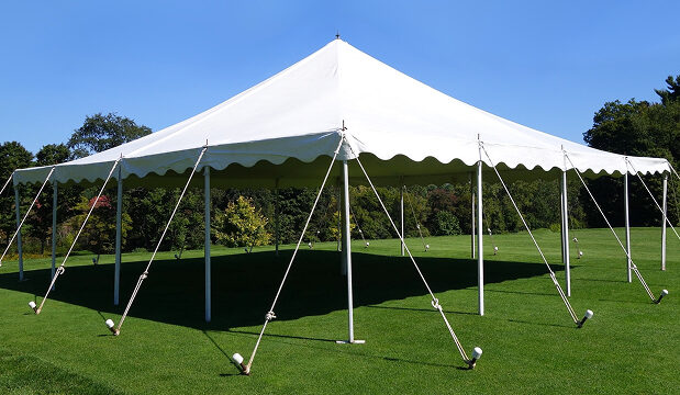 White outdoor tent set up on a grassy field under a clear blue sky.