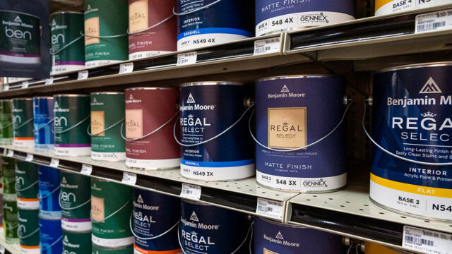 Shelf stocked with assorted paint cans in various colors at a store.