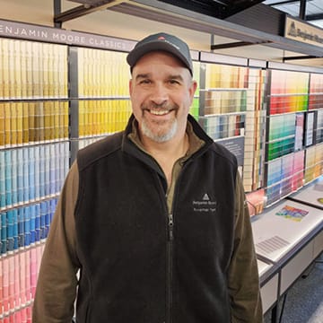 Smiling man standing in front of a display of colorful paint samples at a store.