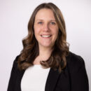 Smiling person in a professional outfit against a plain background.