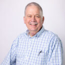 Man in a checkered shirt smiling against a plain background