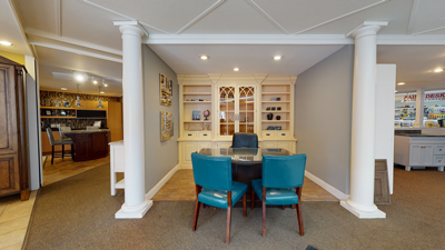 Dining area with a glass table, four teal chairs, and a wooden cabinet display against a gray wall and column.