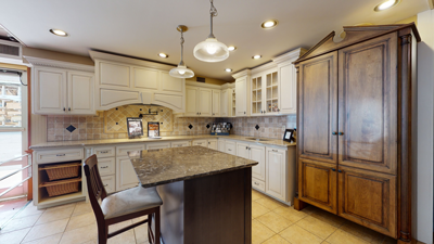 Modern kitchen with granite island, cream cabinets, recessed lighting, and tile backsplash.