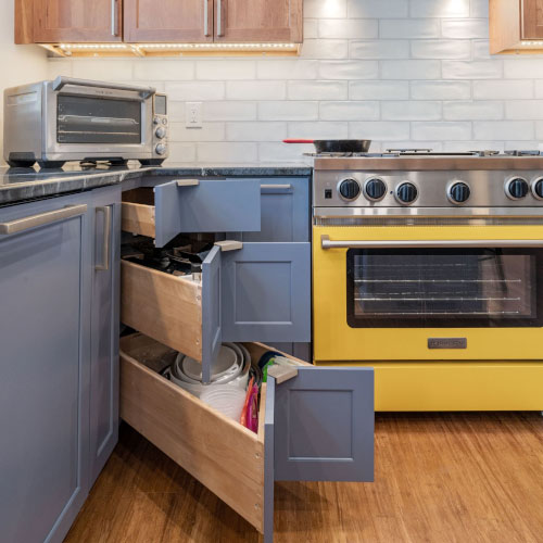 A kitchen features a yellow stove, blue drawers, and a corner cabinet, creating a vibrant and functional space.