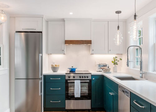 Modern kitchen with white cabinets, stainless steel appliances, teal lower cabinets, wooden floor, and colorful rug.