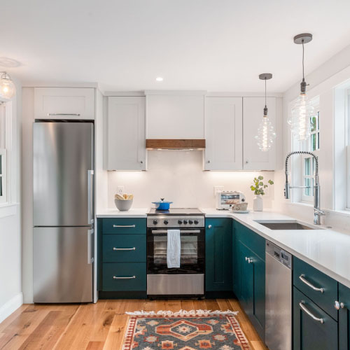 Modern kitchen with white cabinets, stainless steel appliances, teal lower cabinets, wooden floor, and colorful rug.