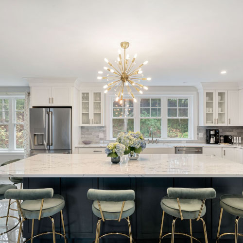 Modern kitchen with large island, chandelier, bar stools, stainless steel appliances, and white cabinetry.