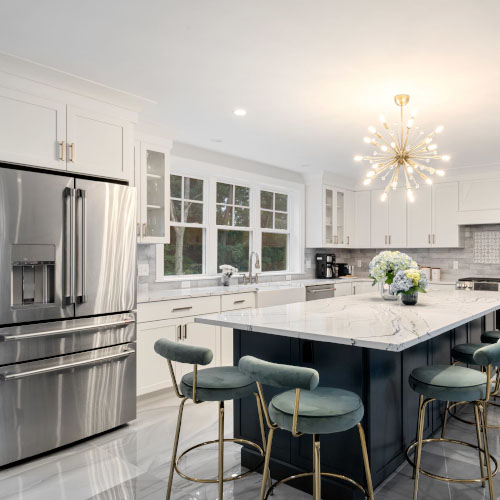 Modern kitchen with stainless steel appliances, large island, green bar stools, and a contemporary chandelier.