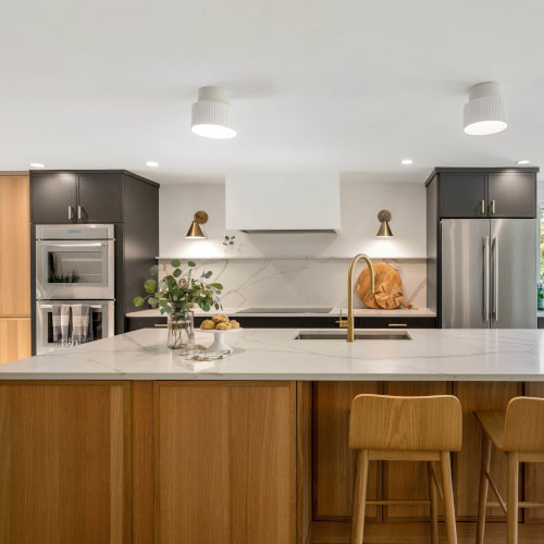 Modern kitchen with wooden island, bar stools, stainless steel appliances, and decorative lights.