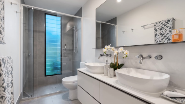 The picture depicts a sleek bathroom with two sinks and a large walk-in shower. There is an orchid between the two sinks and patterned towels hanging on the wall.