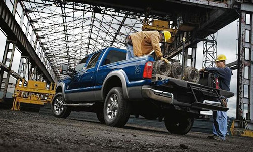 Worker loading pipes onto a blue pickup truck in an industrial warehouse setting