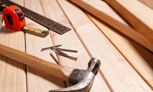 Wooden planks with a hammer, nails, a measuring tape, and a metal ruler on a workbench surface.