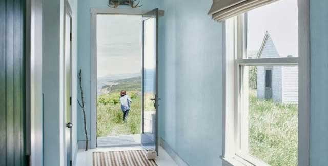 Open door leading to a scenic view with a person walking in a grassy field under a cloudy sky, blue walls and striped rug indoors.