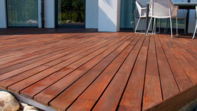 Wooden deck with smooth planks, white chairs, and a modern glass building in the background.