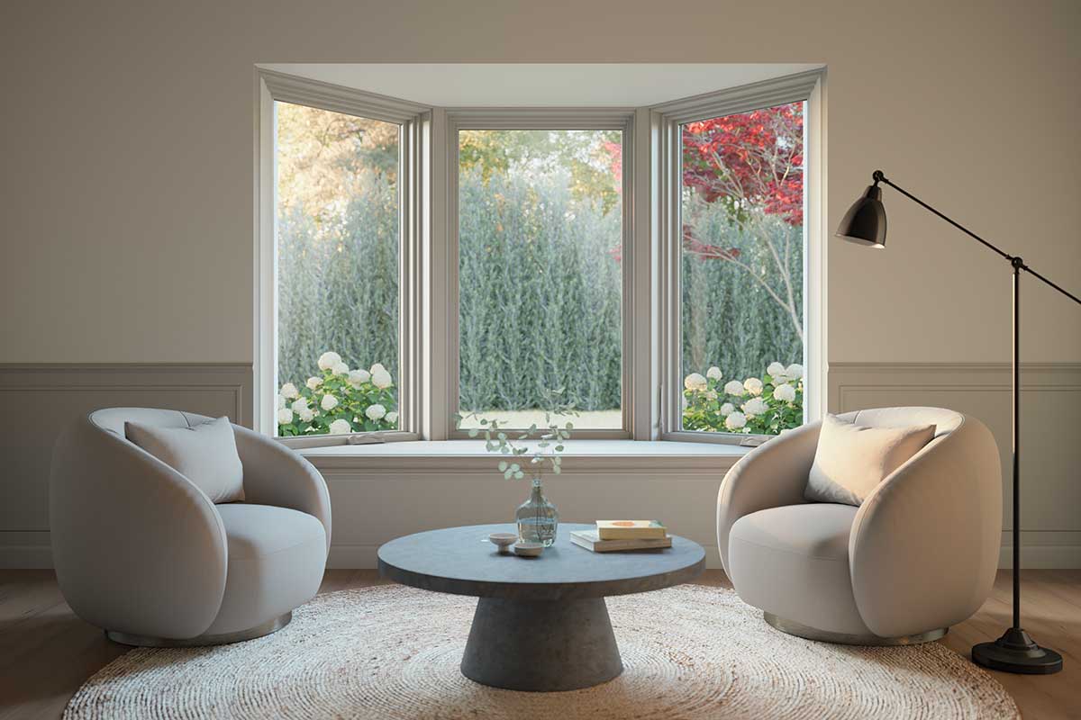 The picture depicts a sitting area with two plush modern seats and a sleek coffee table set in the middle. Behind the seats is a large three panel window that overlooks a garden with hydrangeas.