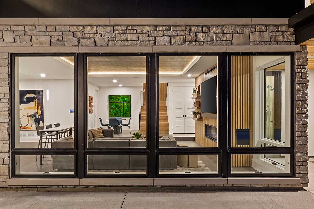 The picture depicts the exterior of four large windows that look into a modern-style living area.