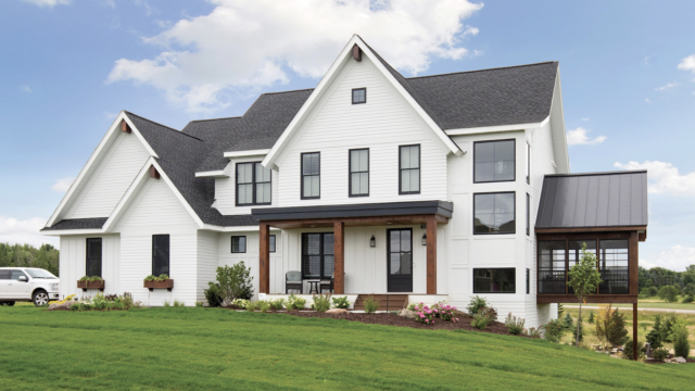 Modern white farmhouse with black trim, large windows, and a manicured lawn under a partly cloudy sky.