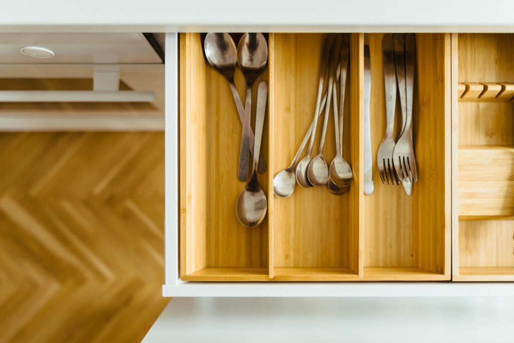 A wooden silverware tray sits in a white drawer with neatly arranged utensils.