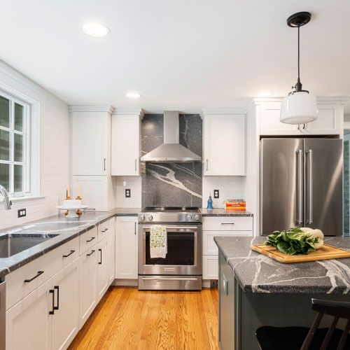 Modern kitchen with stainless steel appliances, white cabinets, black countertops, and a wooden floor.