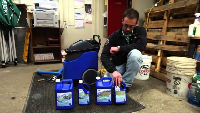 Man kneeling next to blue cleaning equipment and four bottles of cleaning solution in a supply room setting.