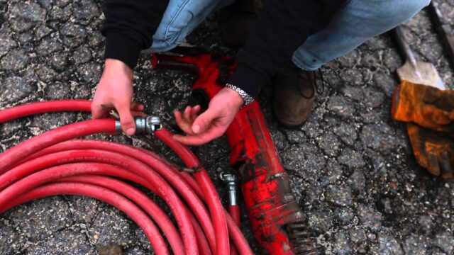 Person checking a red hose connected to a tool on a rough surface.