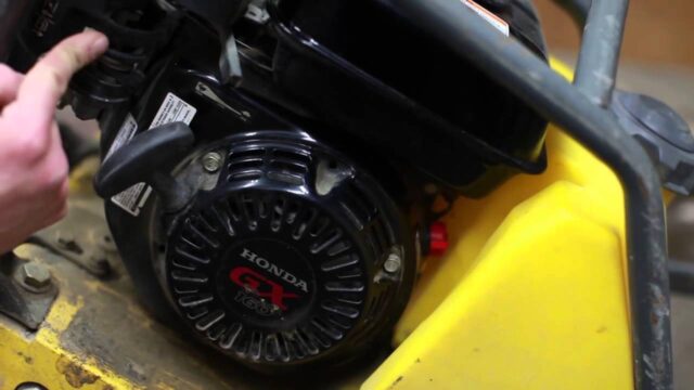 Close-up of a Honda GC engine mounted on a yellow surface, showcasing its intricate design and branding details.
