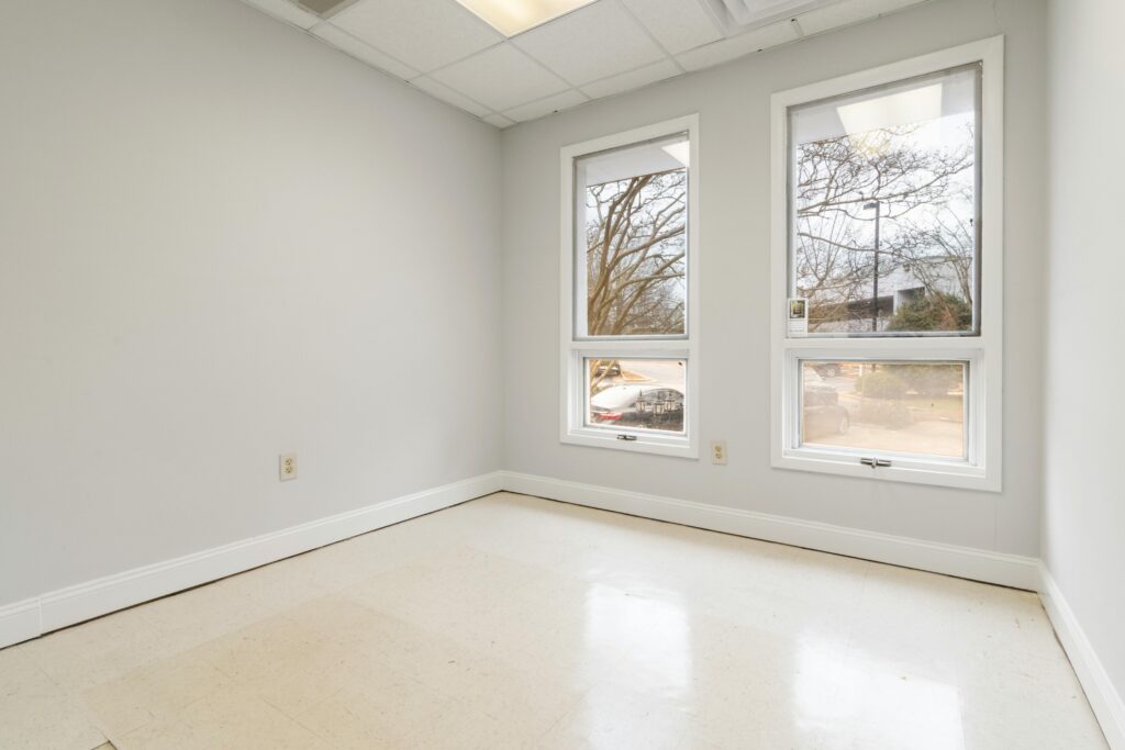 An empty, freshly renovated room features two large windows with two smaller awning-style windows below.