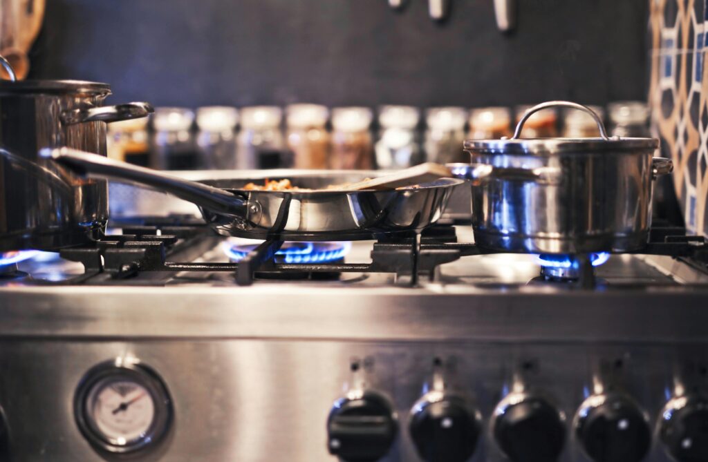 This image depicts a gas stove. Blue flames are shown heating pots and a pan.