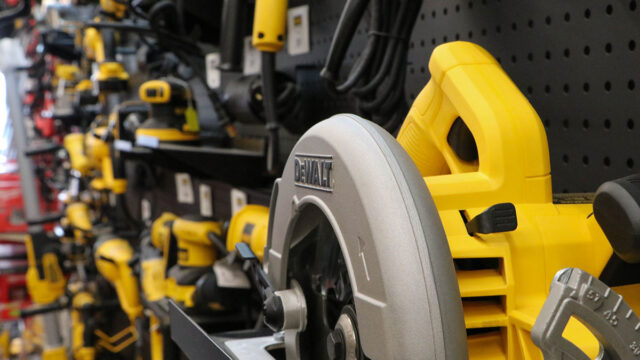 Variety of yellow and black power tools, including a circular saw, displayed on a store shelf with a pegboard background.