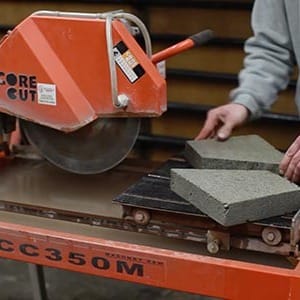 Person using a concrete saw to cut gray concrete blocks on a workbench.