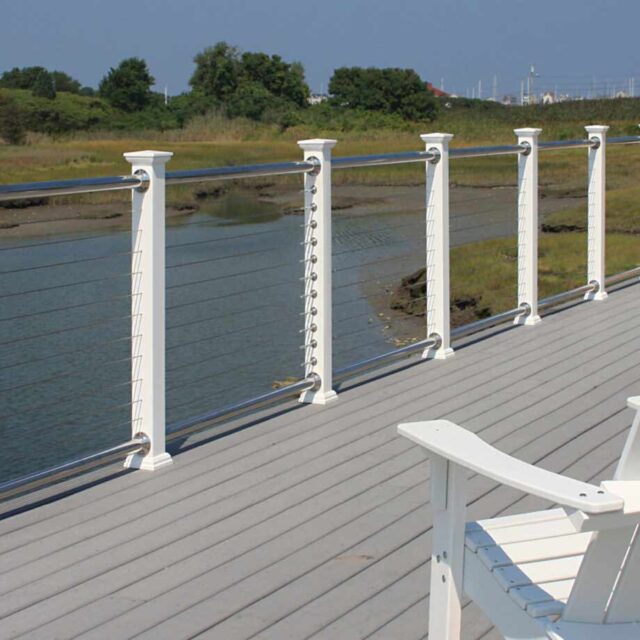 White railing with cable design along a wooden deck overlooking a tranquil river and grassy landscape.