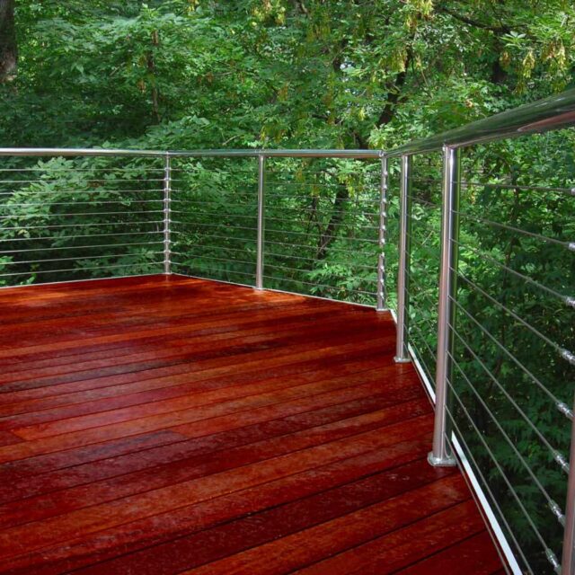 Wooden deck with metal railing surrounded by lush green trees.