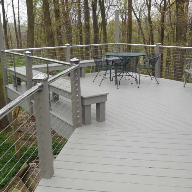 Spacious wooden deck with metal railing and outdoor furniture, surrounded by trees in a serene natural setting.