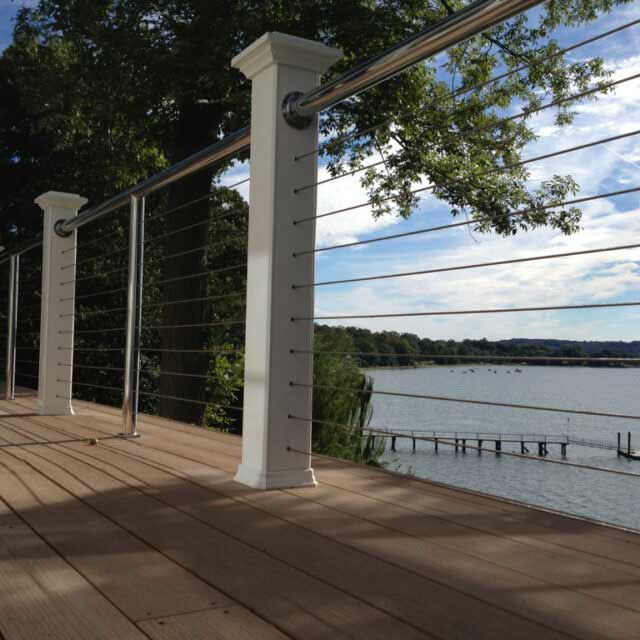Scenic view of a lake from a wooden deck with modern cable railing and trees in the background on a sunny day.