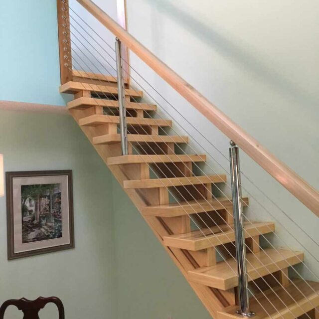 Modern wooden staircase with metal railings in a light green room, featuring a framed painting on the wall.