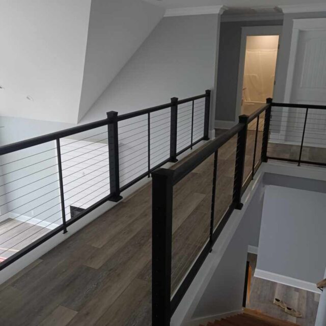 Modern interior with a metal cable railing on a second-floor walkway, featuring wooden flooring and gray walls.