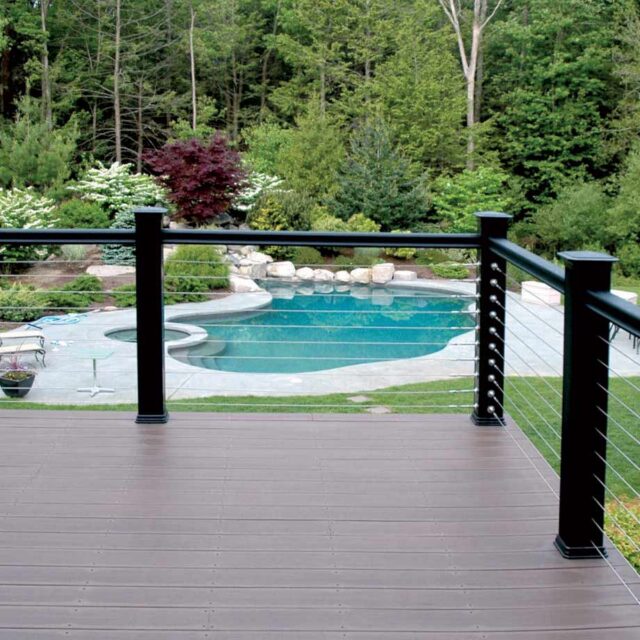 view of swimming pool and hot tub surrounded by greenery from a wooden deck with metal and cable railing