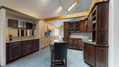 Spacious kitchen showroom with wooden cabinets, a central island, and sample display on the left wall.