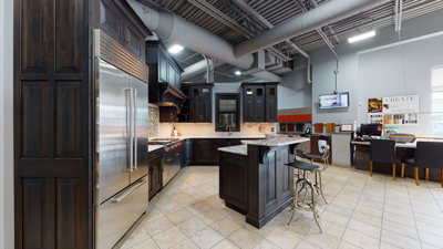 Modern kitchen showroom with dark cabinets, stainless steel appliances, and a central island with chairs.
