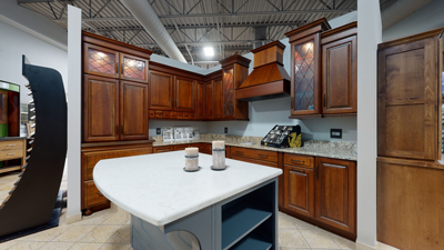 Modern kitchen display with wooden cabinets, marble island, and overhead lighting in a showroom setting.