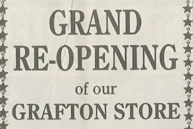 Grand reopening sign announcing the re-opening of a store in Grafton, with bold text on a light background.